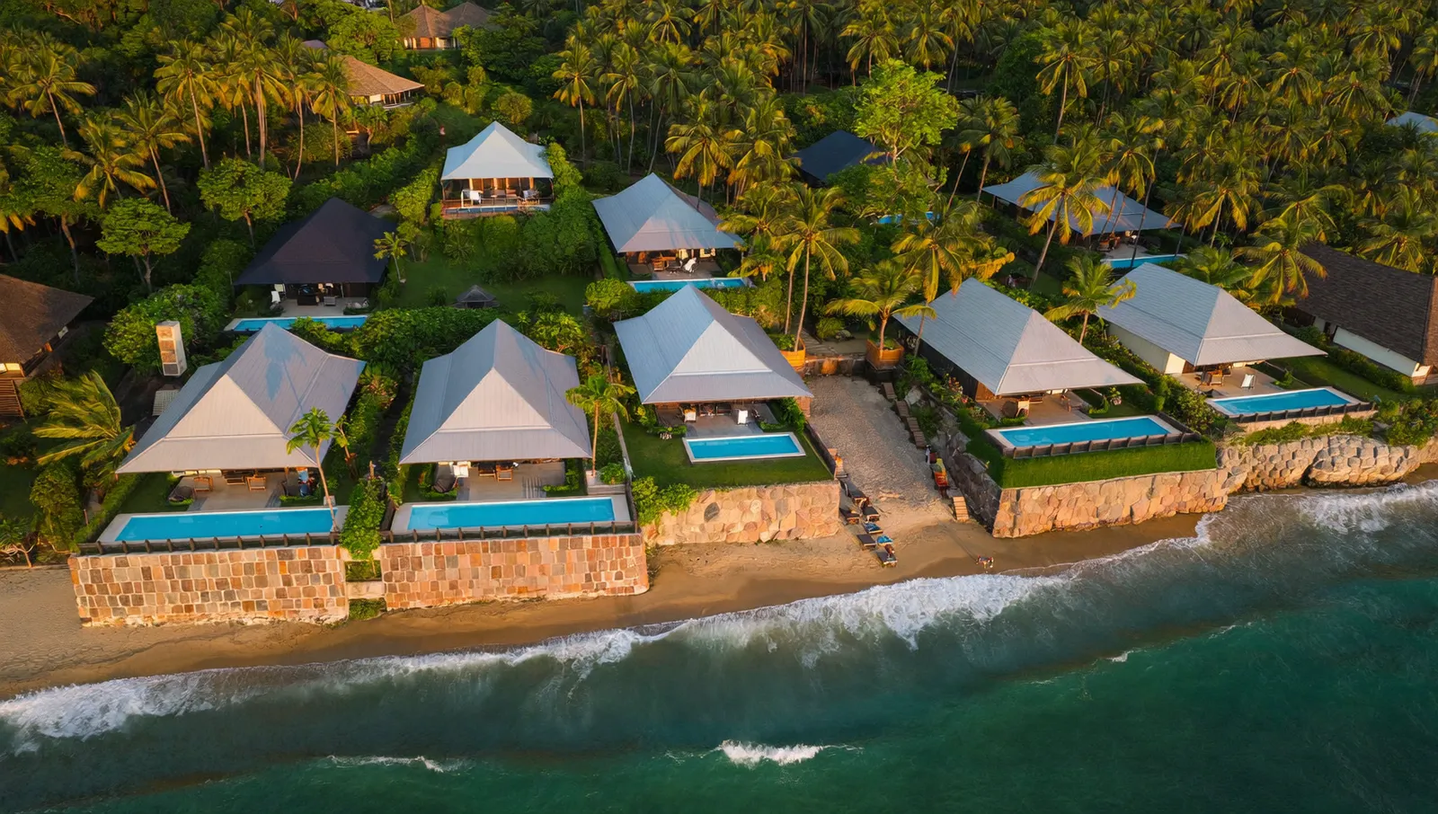 Aerial view of Bali coastal villas with metal roofs and railings near the ocean